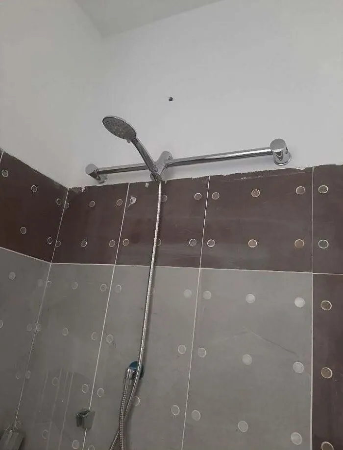Handheld shower head mounted onto a grab bar in a bathroom, showing construction fails.