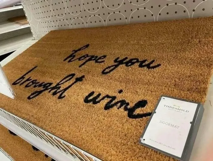 A funny design fail on a doormat with cursive text that looks like hope you brought urine instead of wine.