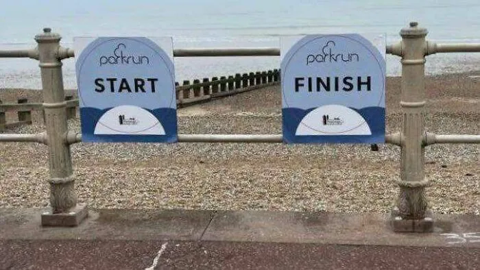 Parkrun start and finish signs placed right next to each other on a fence