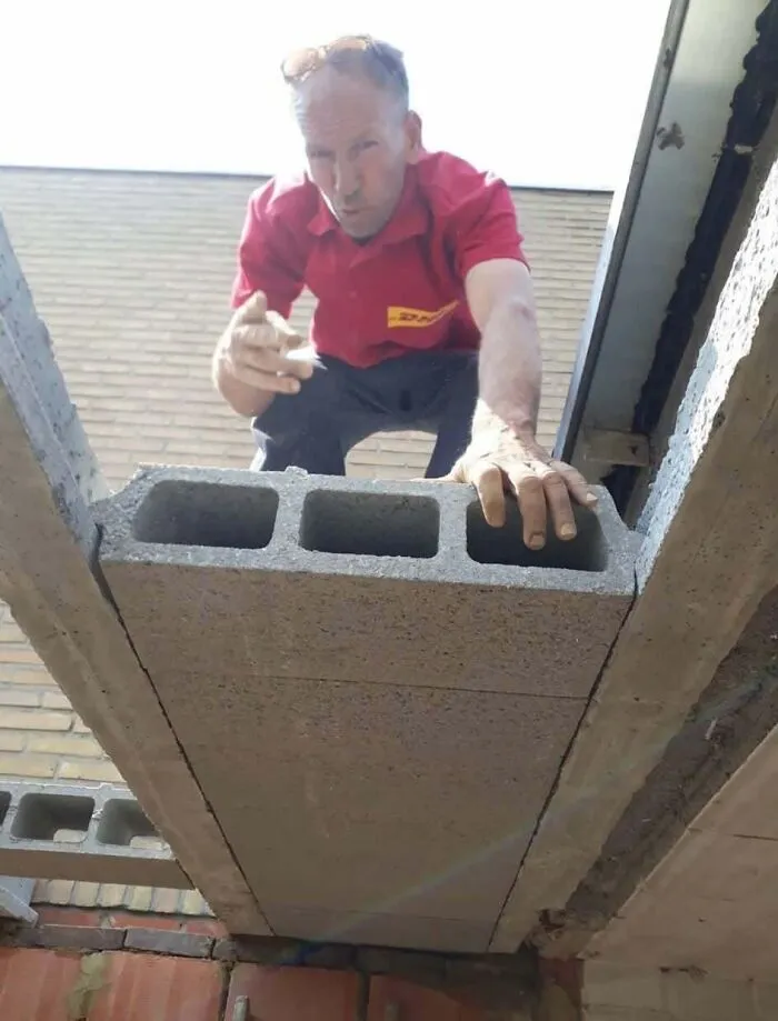 A worker crouching over a cinder block incorrectly placed in a floor gap, an example of obvious construction fails.