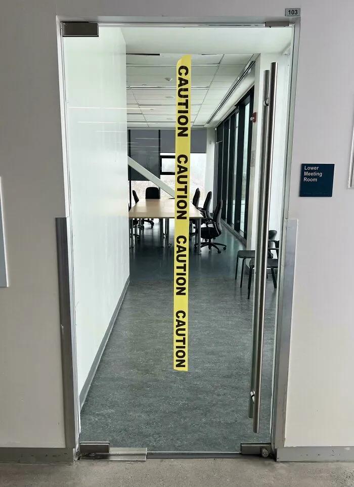 Glass door to meeting room with caution tape stuck vertically across it