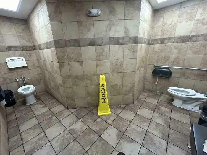 Public bathroom with two toilets facing each other and caution wet floor sign