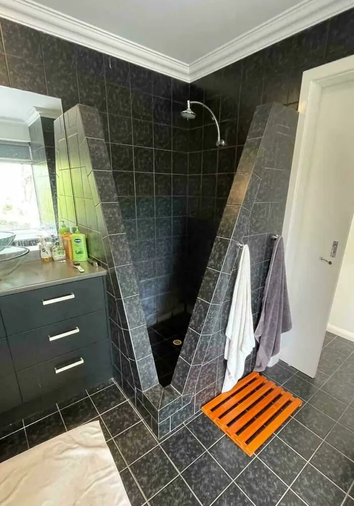 Black tiled shower with narrow triangular entrance and odd design