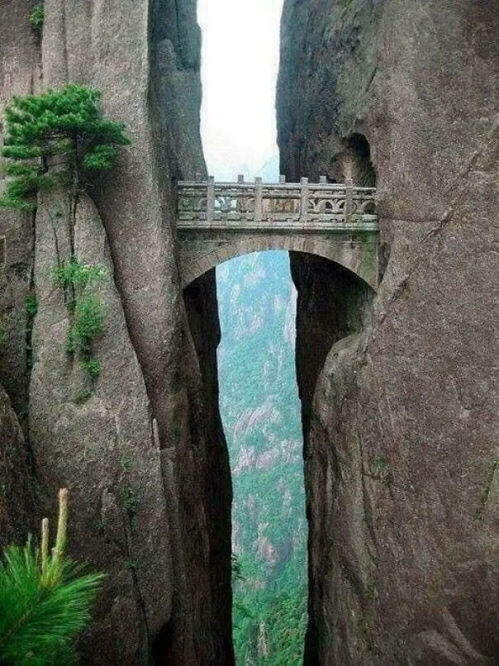 Ancient stone bridge connecting two cliffs surrounded by lush greenery