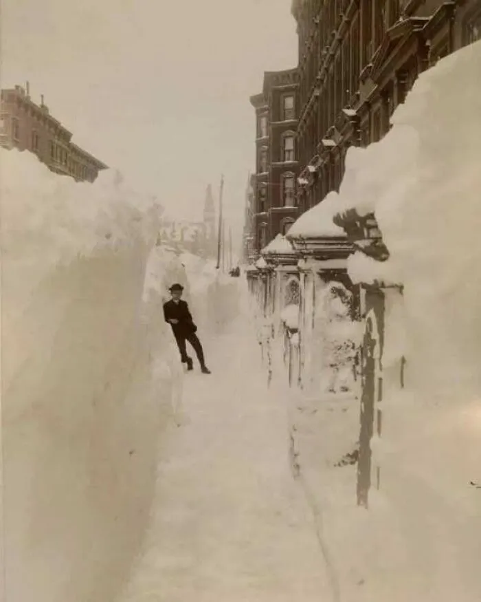 Historic image of a city street buried in deep snow with a man standing in the path