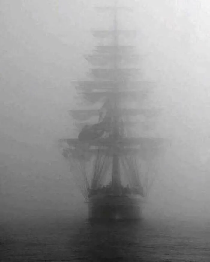 Historic sailing ship faintly visible in fog over water