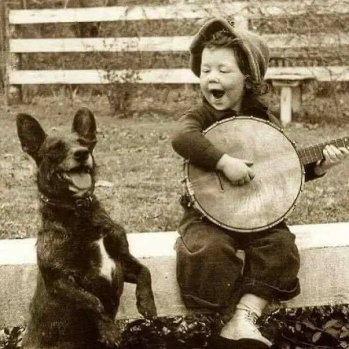 Vintage photo of child playing banjo with happy dog outdoors historic moment