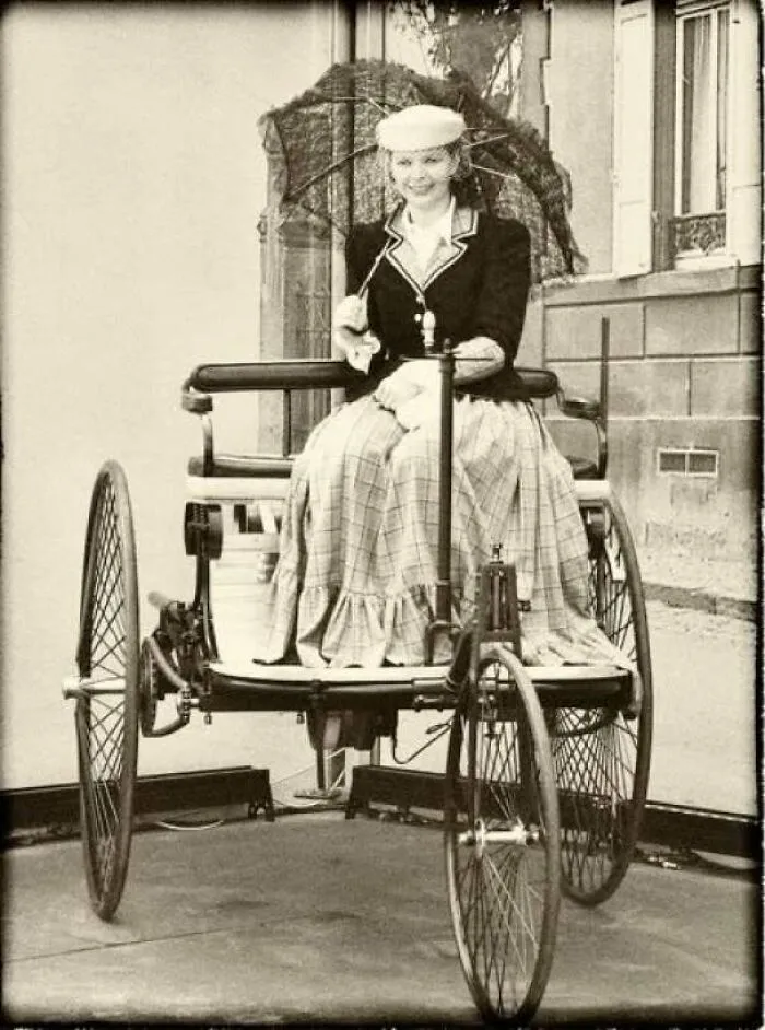 Early vintage photo of a woman riding a historic three-wheeled vehicle