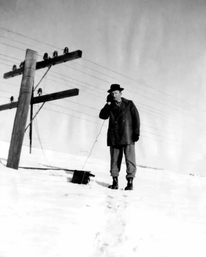Historic image of man using an early telephone device in snowy outdoor environment
