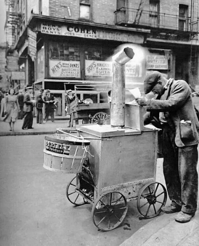Vintage street scene showing man operating a mobile food cart in early 20th century city