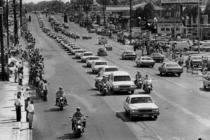 Historical black and white photo of a motorcade procession with crowd
