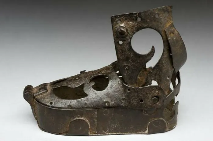 Rusty medieval iron shoes artifact with intricate cut-out patterns