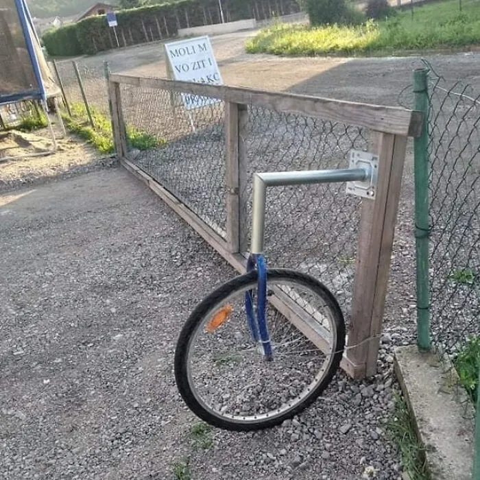 Unusual fence gate supported by a bicycle wheel demonstrating quirky Slavic engineering.