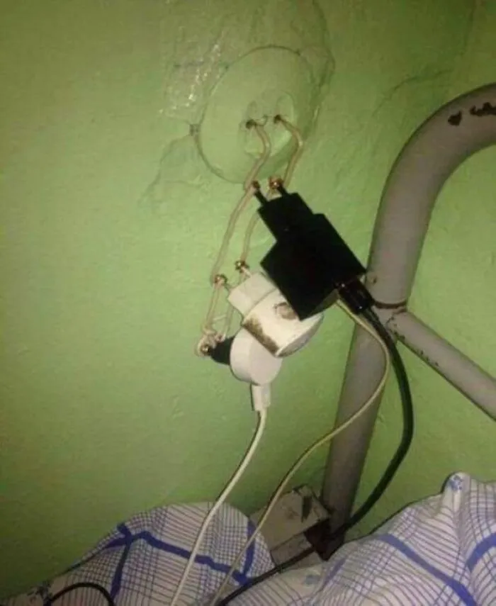 Hazardous homemade electrical wiring setup next to a bed showing dangerous Slavic engineering.