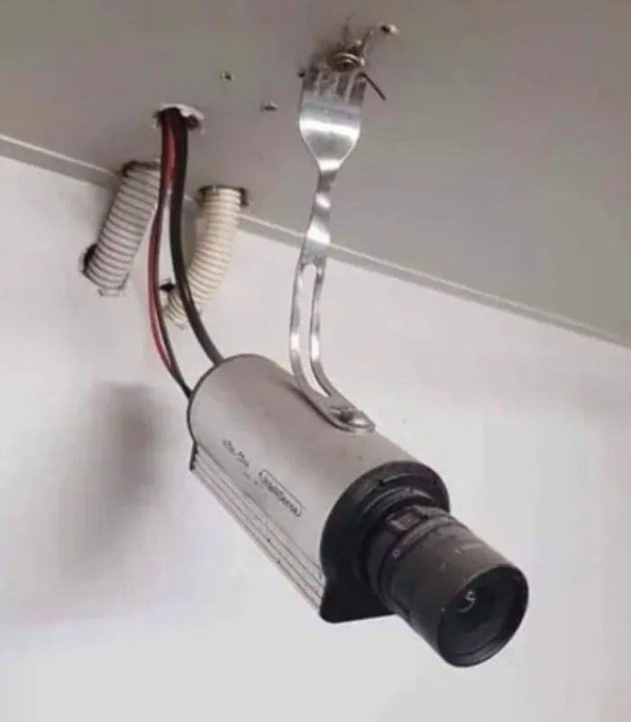 Security camera mounted to the ceiling using a metal eating fork, an unhinged example of Slavic engineering.