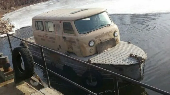 An old van body mounted onto a boat hull floating in water, a unique Slavic engineering fix.