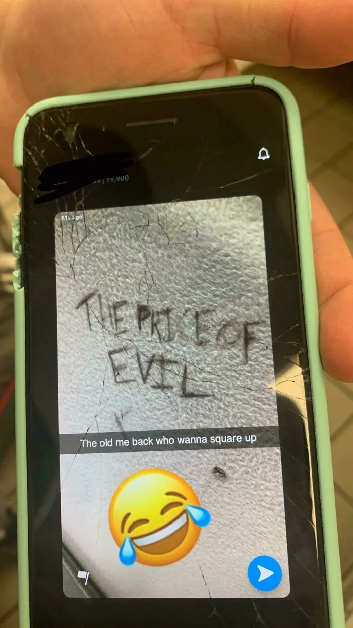 Phone screen with cracked glass showing text The price of evil and laughing emoji