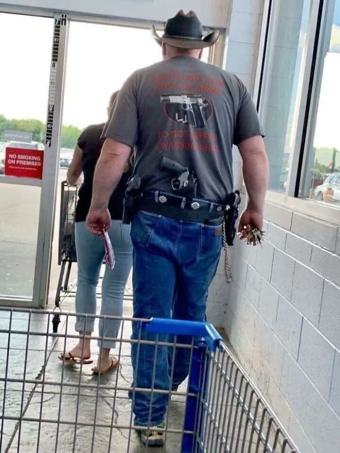 Man wearing gun-themed shirt and holstered firearms at store showing online tough look