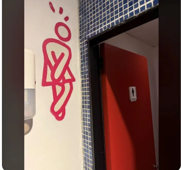 Bathroom wall art showing a person crossing legs near restroom door