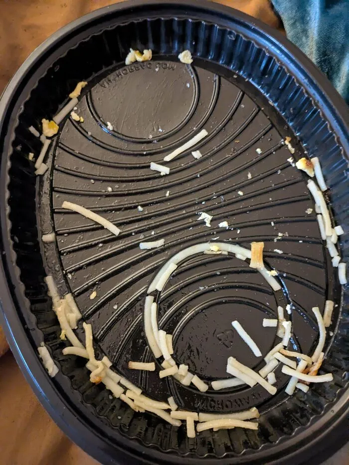 Empty black food container with leftover shredded cheese arranged in circular pattern