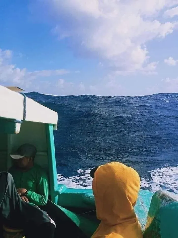 People on boat facing large deep water waves under partly cloudy sky