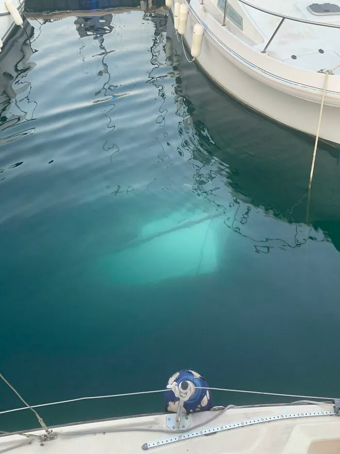 Creepy deep-water photo of a sunken boat visible beneath calm marina water