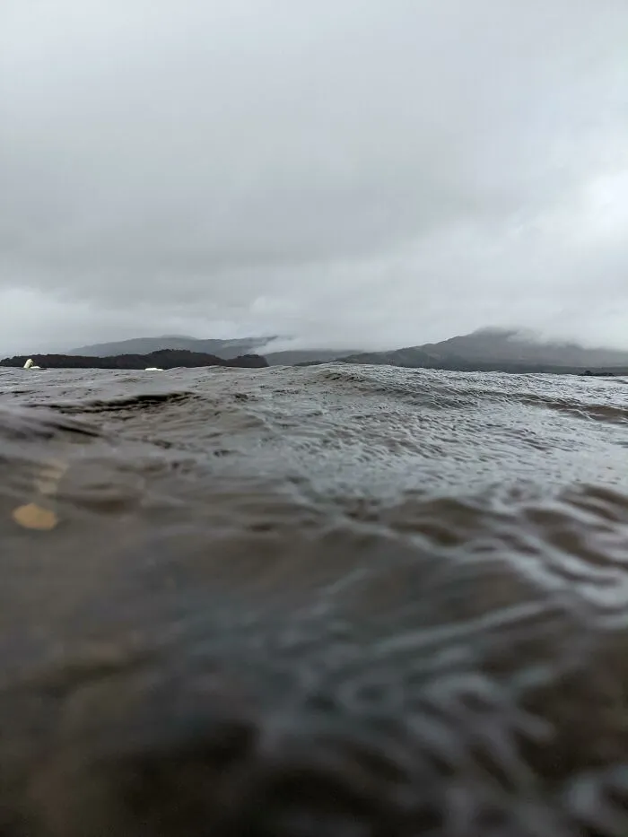 Dark, rippling deep water with obscured mountainous background under cloudy sky