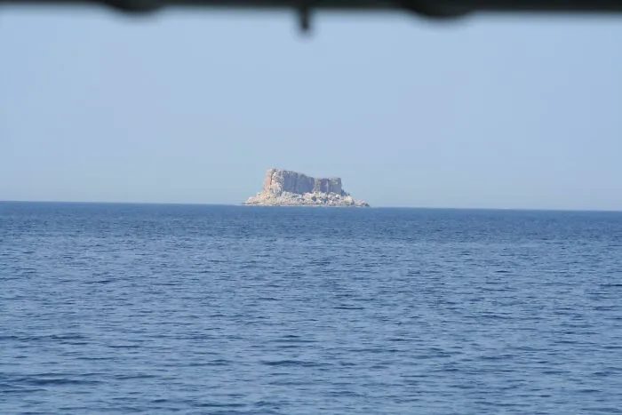 Distant rocky island in calm deep-water sea under clear sky
