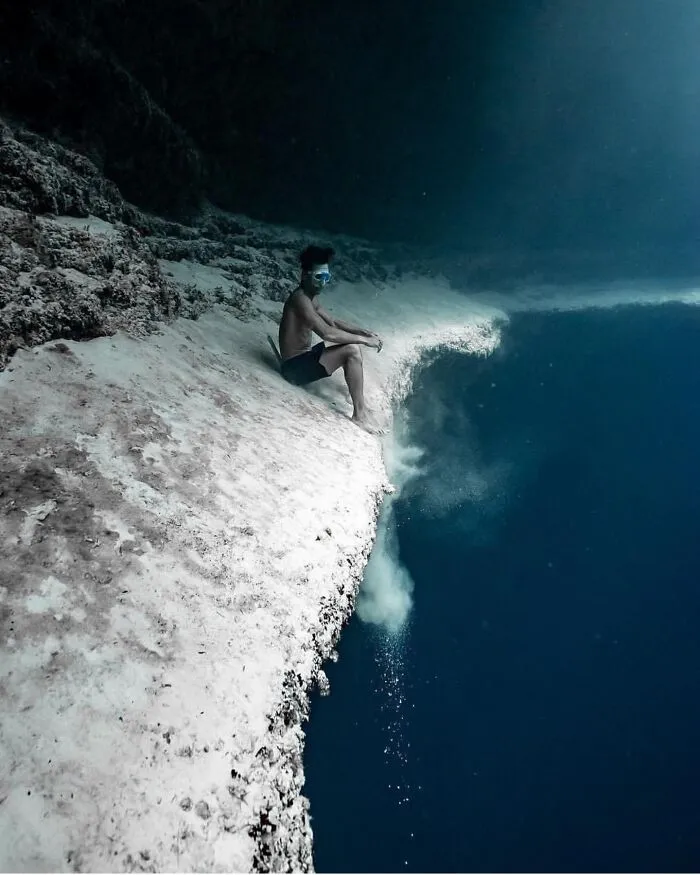 Person sitting underwater beside a deep-water abyss cliff