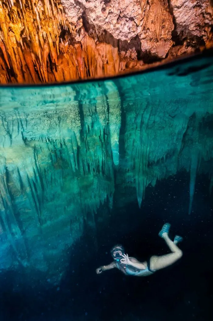 Underwater cave with diver exploring stalactites and clear blue water