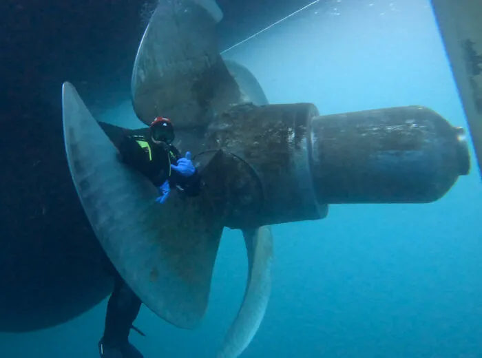 Diver next to large ship propeller in deep-water environment