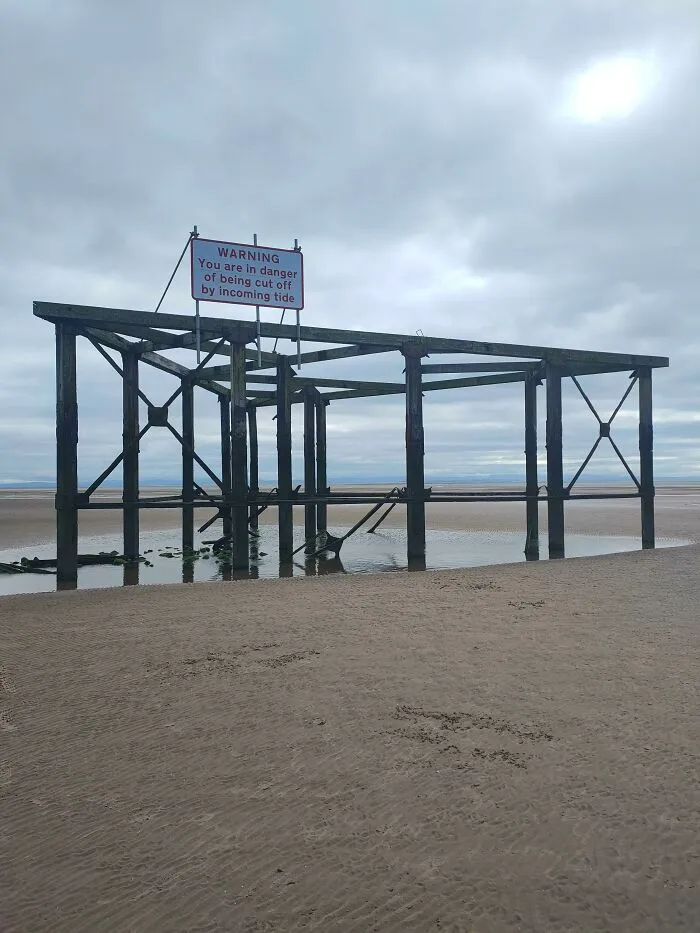 Warning sign on a wooden structure about incoming tide danger on a sandy beach