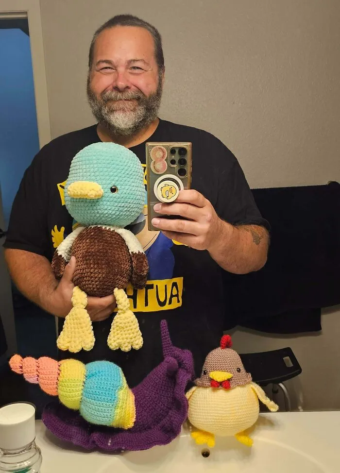 Man holding crochet plush toys of duck, caterpillar, and chicken