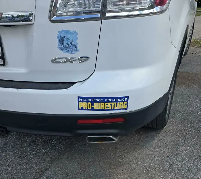 A blue bumper sticker supporting science choice and pro-wrestling on a white car.