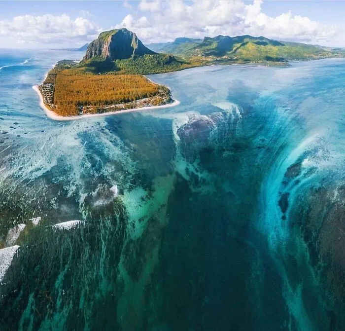 Aerial view of underwater waterfall illusion near island in a creepy deep-water photo