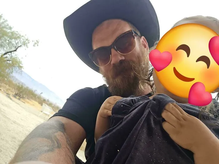 A proud dad wearing a cowboy hat and sunglasses holding his young child outdoors in a loving moment.