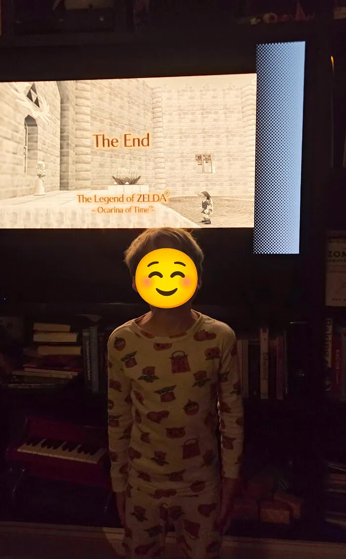 Child standing happily in front of a TV displaying The End of Zelda, showing memorable dads moments.