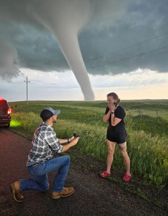 Man proposing to a woman outdoors with a massive tornado behind them making your eyes play tricks