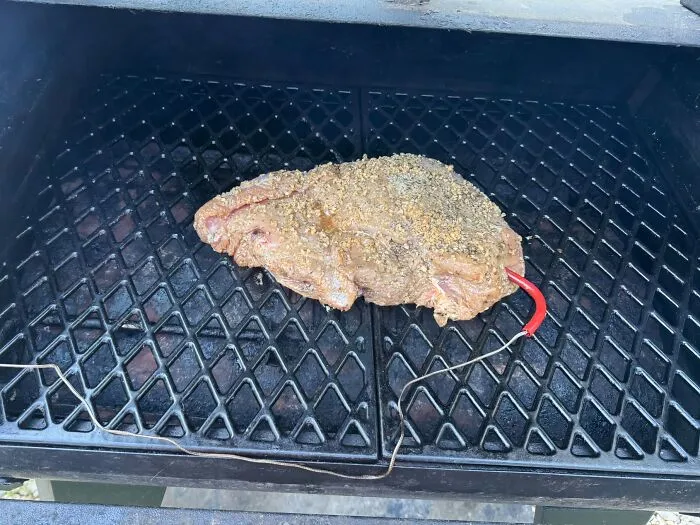 Seasoned meat on a grill grate with a temperature probe creating an optical illusion