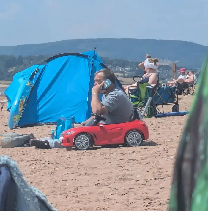 A man sitting in a tiny toy car at the beach among funny photos that play tricks on your eyes.