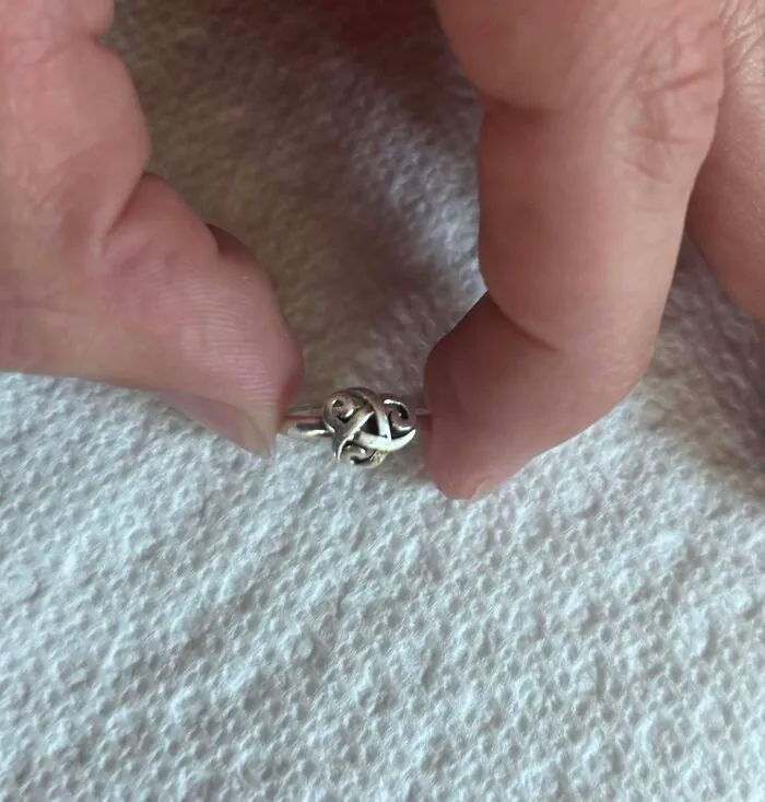 A hand holding a small, intricate silver ring, reminiscent of real-life photos with a horror movie feel.