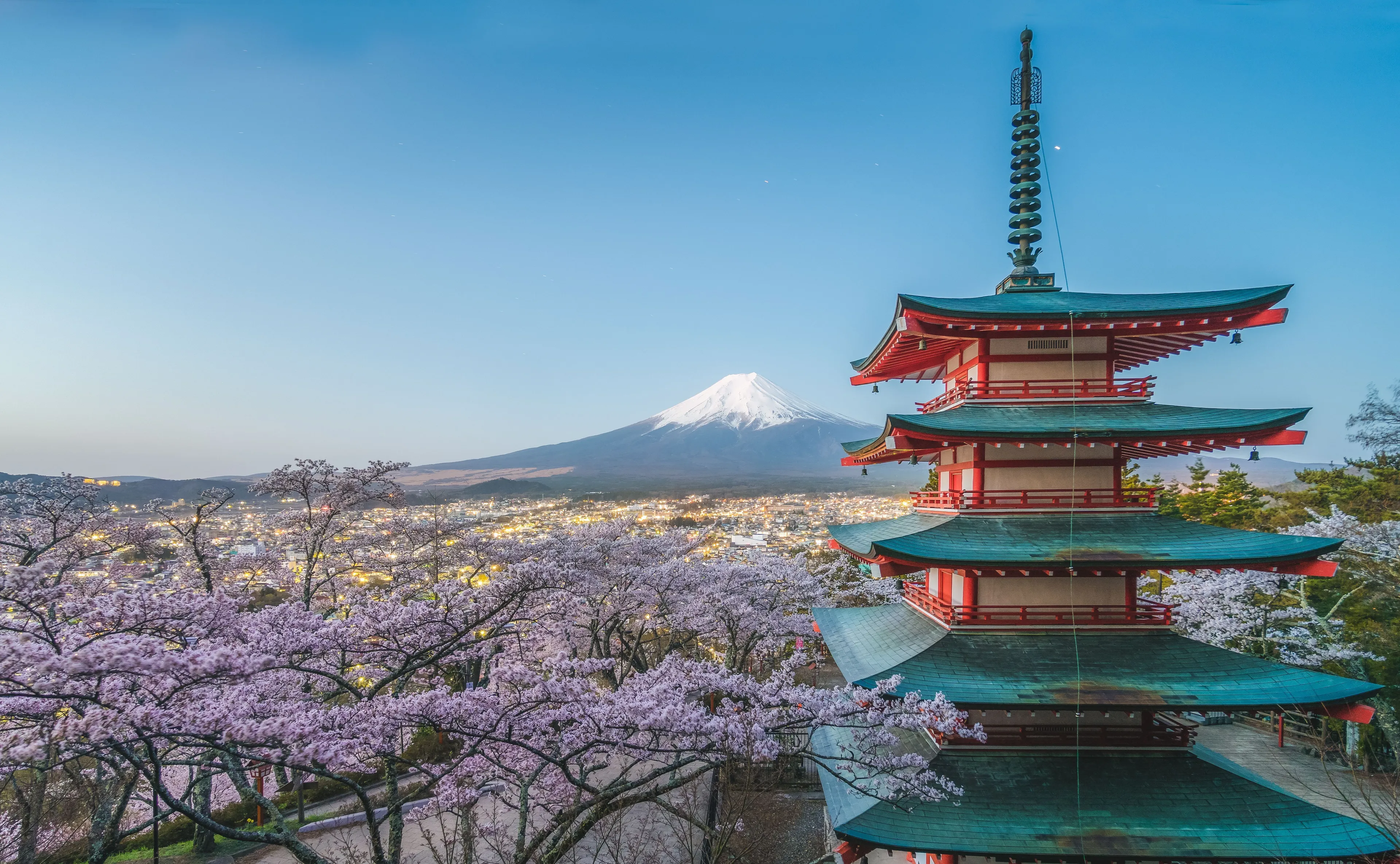 A red pagoda surrounded by cherry blossoms with Mount Fuji in Japan in the background.