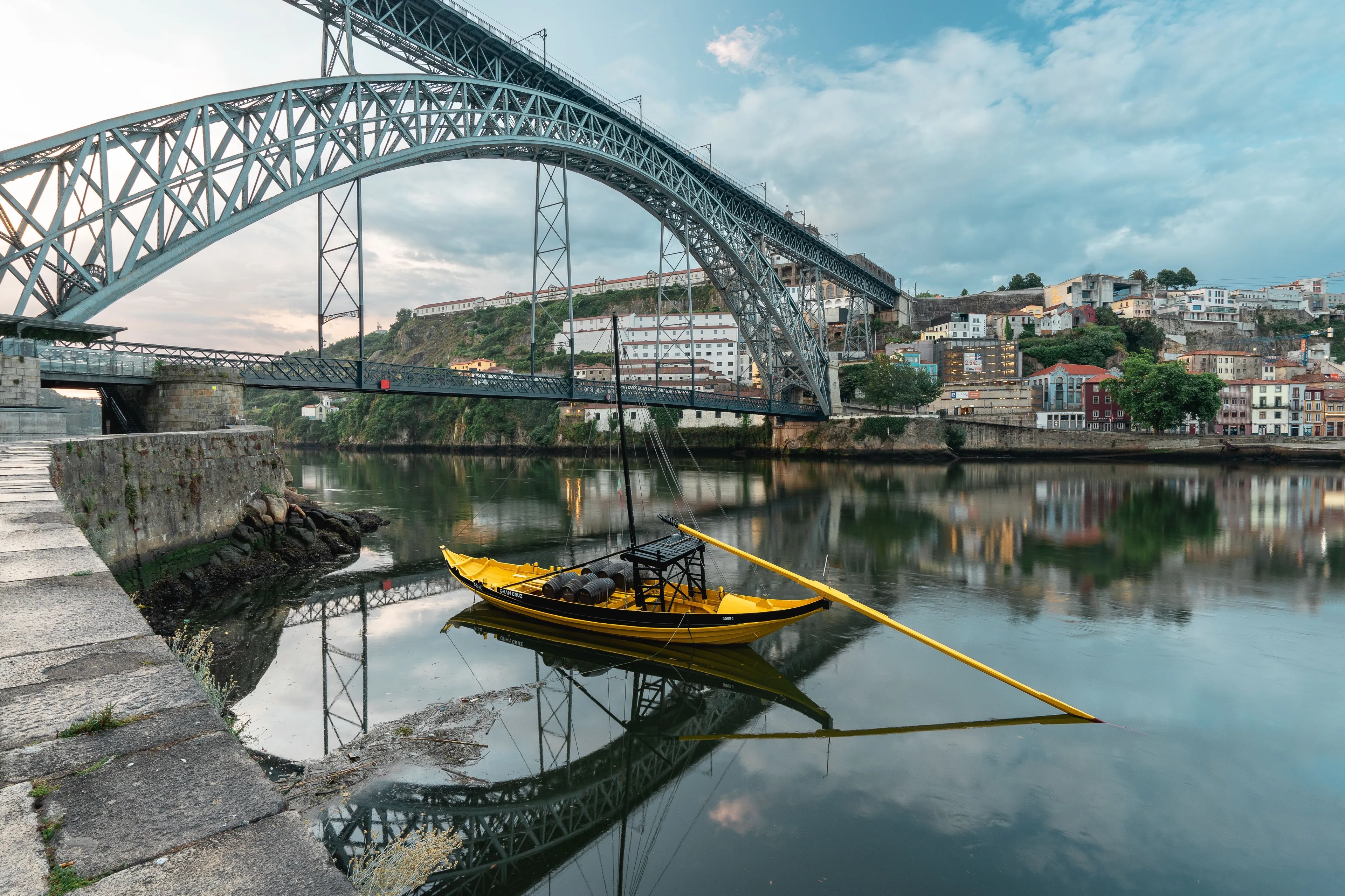 A traditional yellow boat on a river in Porto with a grand arched bridge in the background.