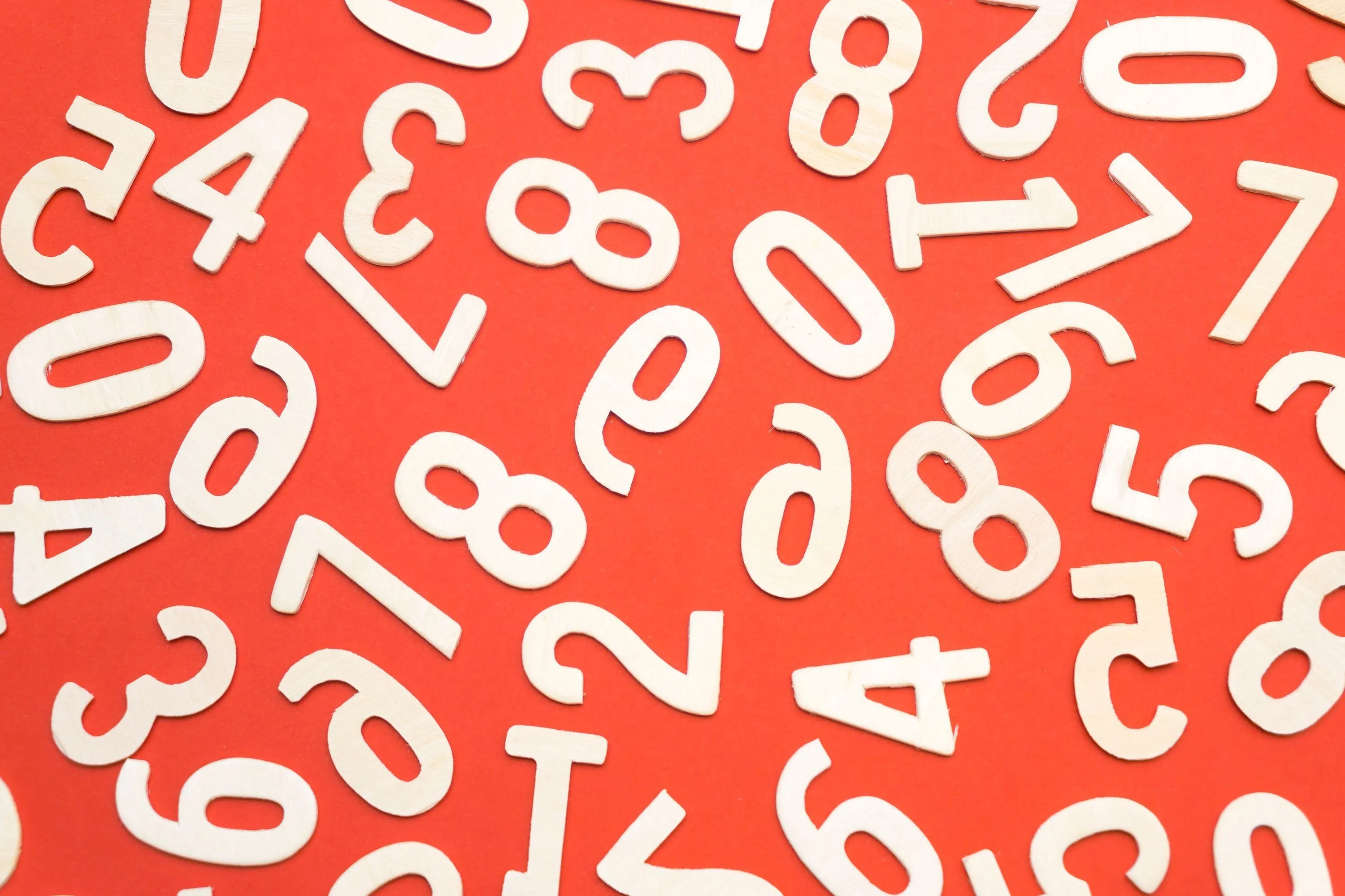 A vibrant pattern of white wooden numbers scattered across a bold red background.