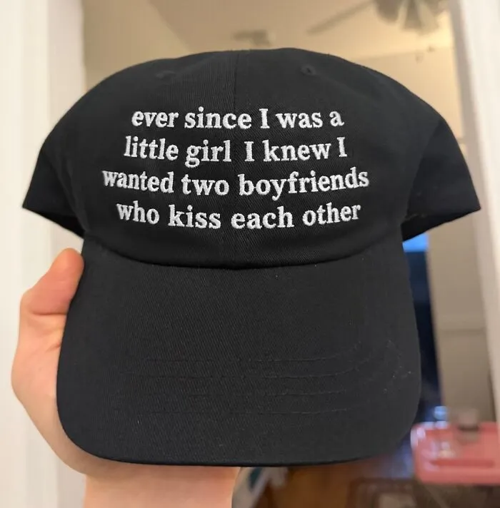 Black baseball cap with white embroidered text about having two boyfriends who kiss.