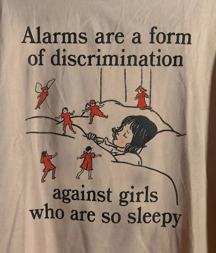 A hilarious t-shirt with a vintage illustration of a sleeping girl surrounded by small figures and text about alarms.
