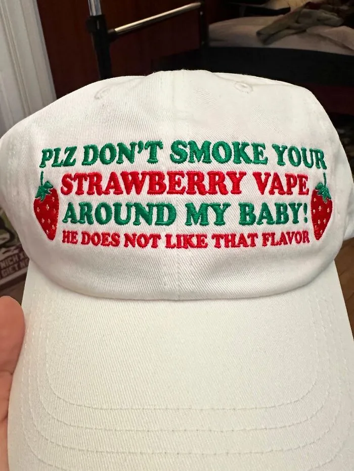 A white cap with embroidered text about strawberry vape flavor and two small strawberry illustrations.