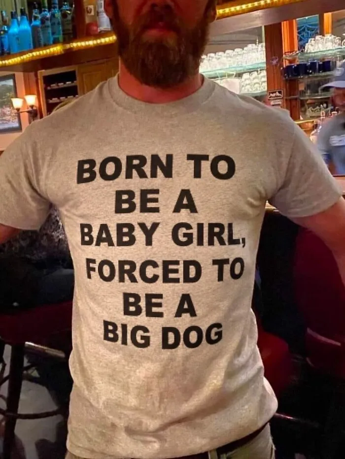 Bearded man wearing a hilarious t-shirt that says Born to be a baby girl, forced to be a big dog.