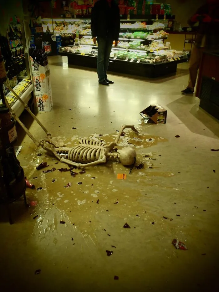 A skeleton lying on a store floor near spilled beer bottles, funny Halloween didn’t go as planned moment
