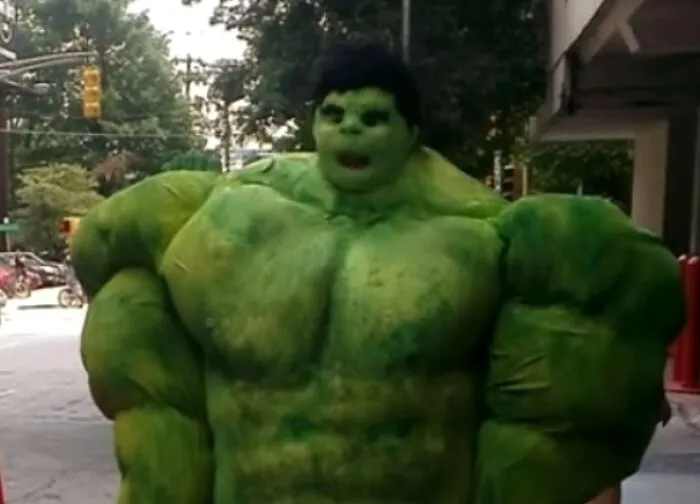 Person wearing a giant, disproportionate green Hulk muscle suit for Halloween